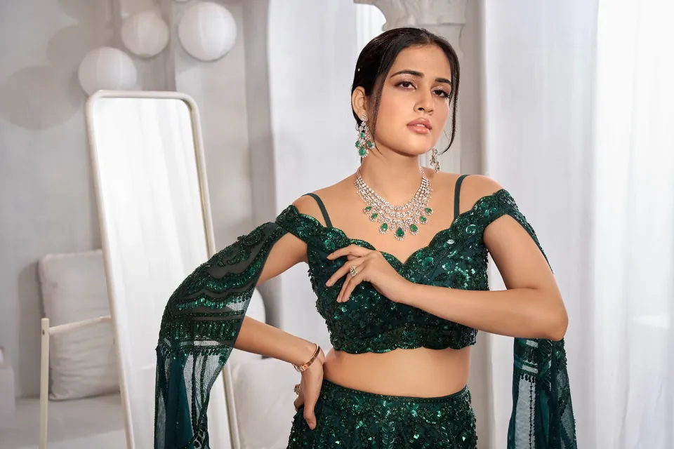 Model seated in green sequins, wearing a diamond and green-stone necklace, bracelet and rings