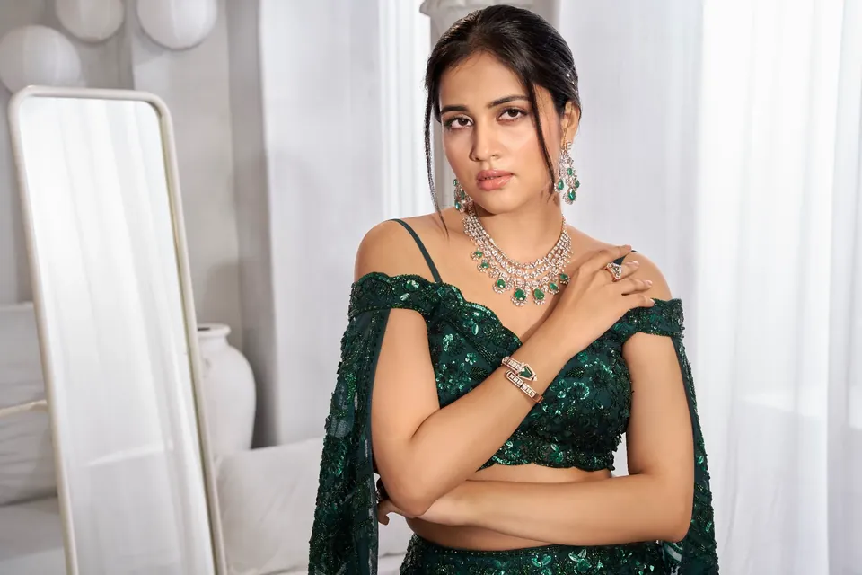 Close portrait in green, hand resting on the shoulder to show rings and a diamond necklace