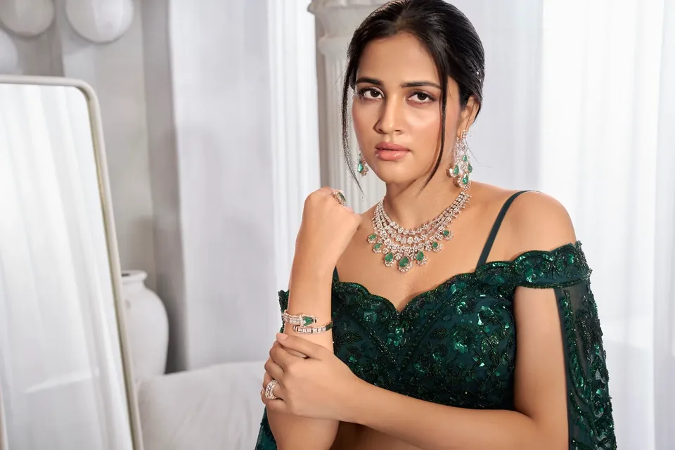 Model in a deep green off-shoulder lehenga wearing a diamond necklace with green drops and matching earrings
