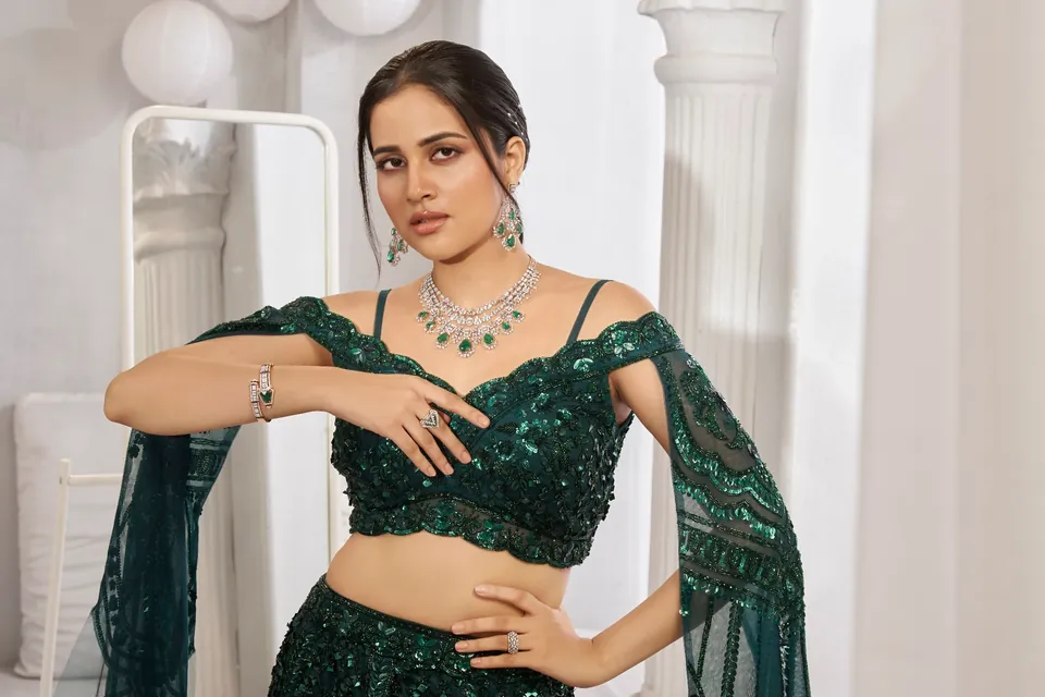 Model in a green lehenga with arms folded, showing a necklace, bracelet and cocktail ring