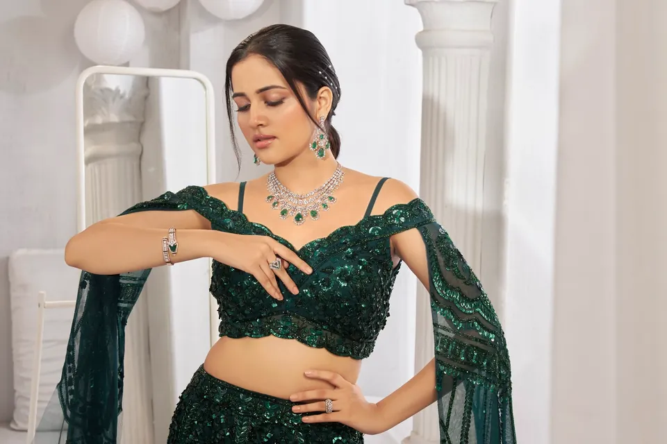 Model looking down in a green lehenga, wearing a diamond necklace with green drops