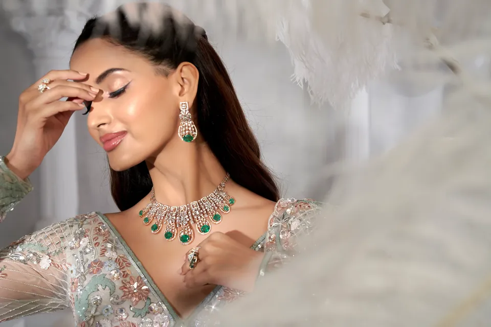 Model with a hand at the brow, wearing a diamond and green-stone necklace