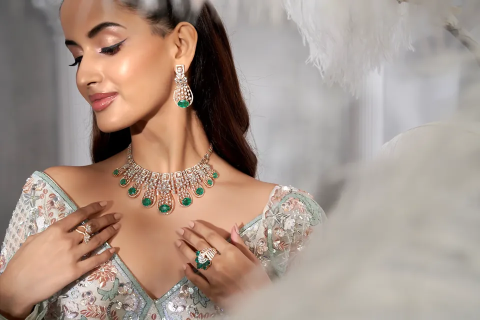 Model looking down with hands at the neckline, showing rings and a green-drop necklace