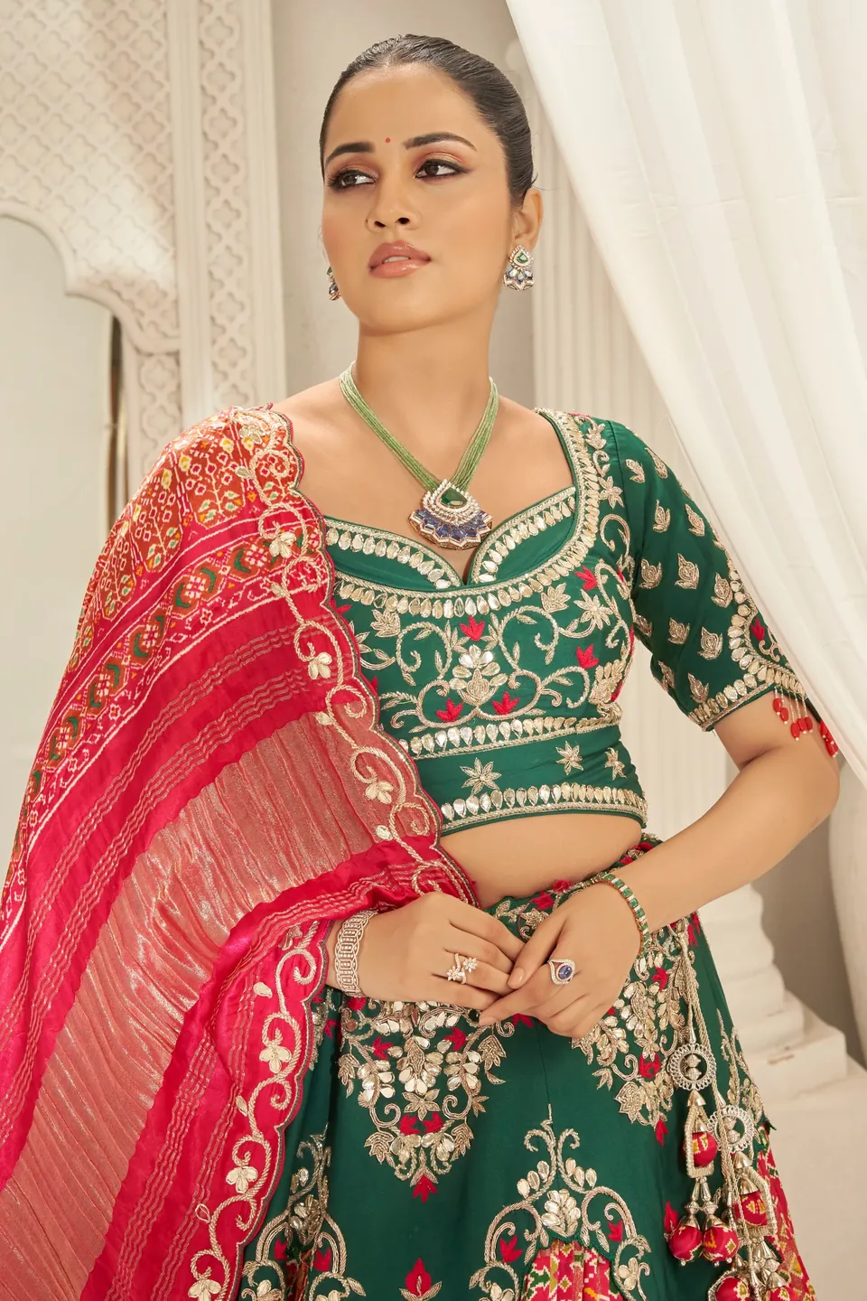 Model in green and crimson wearing a long necklace, bracelet and rings