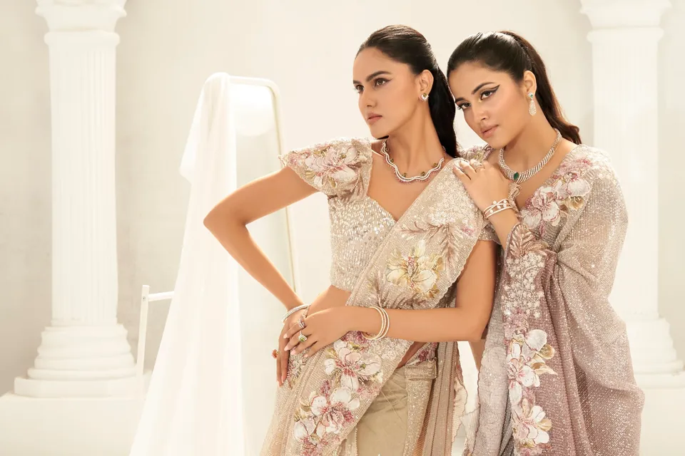 Two models in blush floral saris posed together in a white set