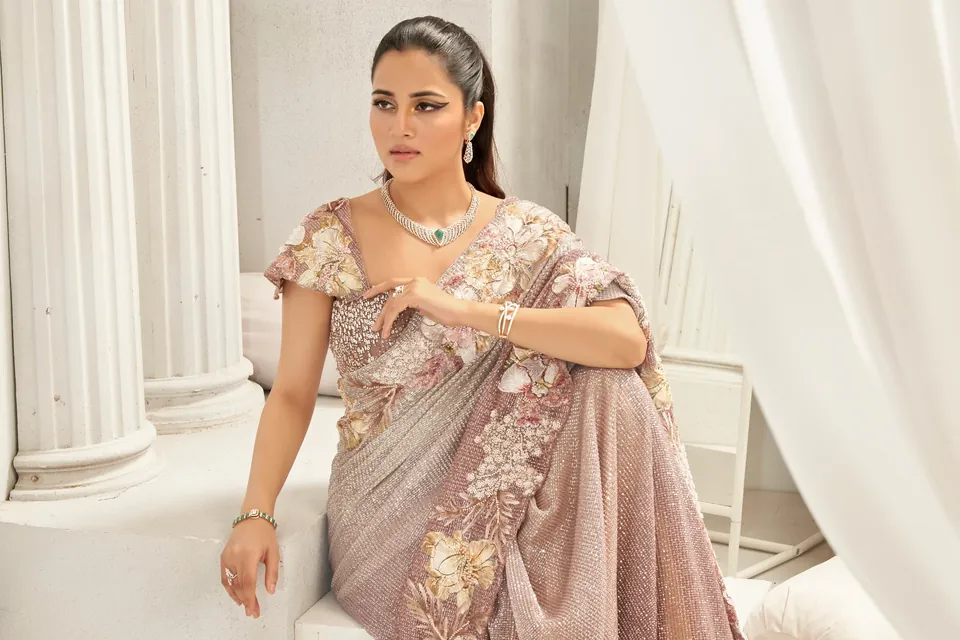 Model seated in a mauve sequinned sari, wearing a diamond necklace with a green stone