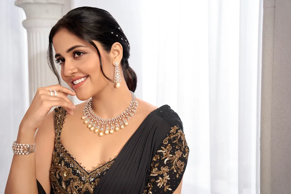 Smiling model in black with a pearl-drop necklace, long earrings and rings