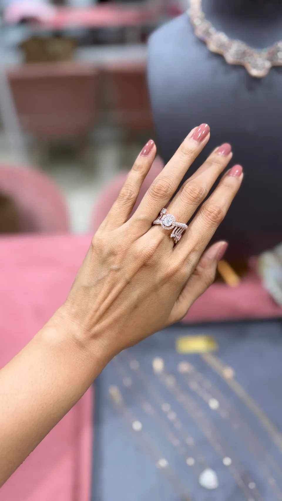 A hand wearing a sculpted rose-gold diamond ring in front of a necklace display